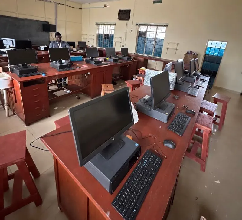 Rows of desktop computers set up on wooden benches in a school computer lab